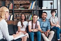 A family of four sits with a therapist